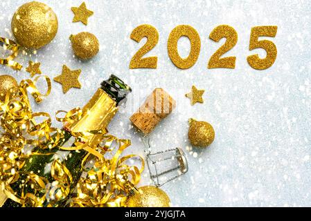 Flasche Champagner mit goldenen weihnachtskugeln, goldenen Sternen und 2025 in goldenen Zahlen auf einem schneebedeckten Hintergrund. Silvesterfeier Konzept Hintergrund Stockfoto