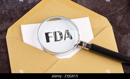 FDA, Worte auf Holzblöcken. Business Concept, FDA geschrieben auf einem leeren Blatt auf einem Briefumschlag durch eine Lupe, ein konzeptionelles Foto. Stockfoto