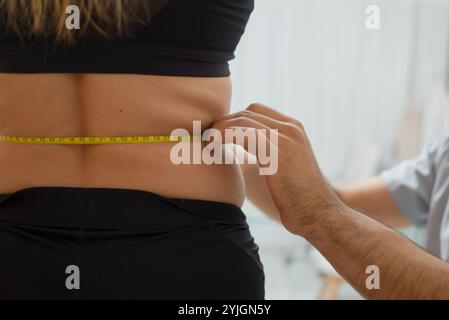 Medizinische Ernährungsberaterin in einem grauen Hemd misst die Taille einer Frau mit einem Maßband. Nahaufnahme. Stockfoto