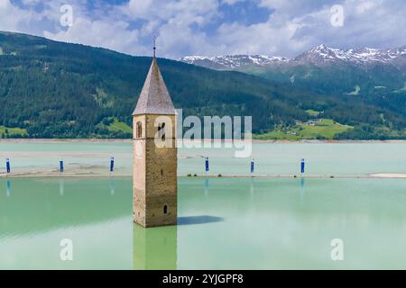 CURON VINSCHGAU, ITALIEN – 28. AUGUST 2024: Aus dem Wasser des Reschensees erhebt sich der berühmte Glockenturm der untergetauchten Vinschgau-Kirche Stockfoto