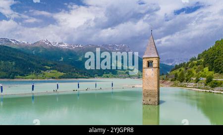 CURON VINSCHGAU, ITALIEN – 28. AUGUST 2024: Aus dem Wasser des Reschensees erhebt sich der berühmte Glockenturm der untergetauchten Vinschgau-Kirche Stockfoto