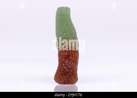 Cola-förmige gummiartige Bonbons und ein mit Zucker gefüllter Holzlöffel auf einem Holztisch vor weißem Hintergrund, die Süße und Leckereien aus nächster Nähe hervorheben Stockfoto