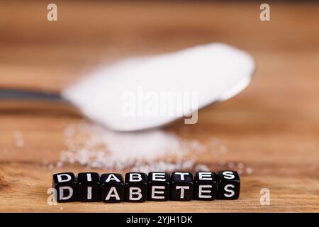 Ein Metalllöffel voller Zucker und Buchstabenwürfel mit der Schreibweise „Diabetes“ ruht auf einem alten Holztisch und symbolisiert Gesundheitsrisiken und Ernährungsbewusstsein Stockfoto