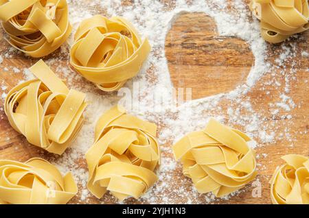 Die Nester der Tagliatelle sind auf einem Holzbrett angeordnet, das mit Mehl bestreut ist und eine Herzform bildet Stockfoto