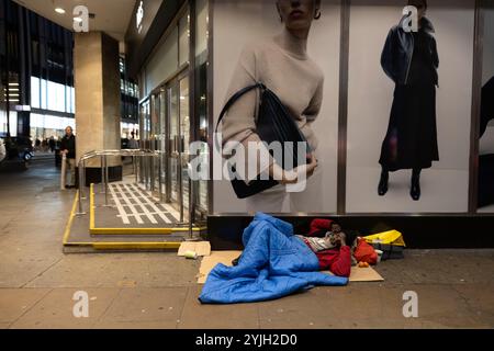 Obdachloser Mann schläft unter einer Damenmodewerbung vor Marks & Spencers Marble Arch Flagship Store im Zentrum von London, England, Großbritannien Stockfoto