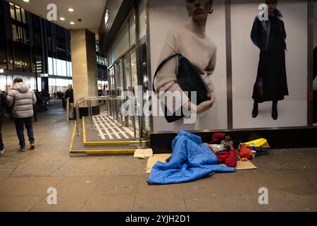 Obdachloser Mann schläft unter einer Damenmodewerbung vor Marks & Spencers Marble Arch Flagship Store im Zentrum von London, England, Großbritannien Stockfoto