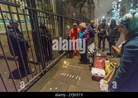 London, Großbritannien. Januar 2018. Bewaffnete Polizisten, die die US-Botschaft bewachen, sprechen mit den Demonstranten, während sie sich auf die Mahnwache bei Kerzenlicht vorbereiten, die den 16. Jahrestag des illegalen Folterlagers in Guantanamo Bay begeht, wo noch 41 Gefangene festgehalten werden, die hauptsächlich auf unbestimmte Zeit ohne Anklage oder Gerichtsverfahren festgehalten werden und die meisten mit dauerhaften Verletzungen durch Folter, die ihre Freilassung für die US-Behörden (und möglicherweise Großbritannien) peinlich machen würden. Die Demonstranten zündeten vor dem Botschaftszaun Kerzen an, in denen sie „GITMO“ schrieben, und standen dann mit Kerzen und großen Fotos der 41 verbliebenen Häftlinge, die meisten zeigten ihnen mehr Stockfoto