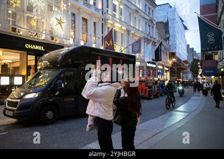 Touristen halten an und machen Fotos von den Weihnachtsfenstern und Weihnachtslichtern entlang der Old Bond Street, Mayfair, im Zentrum von London, England, Großbritannien Stockfoto