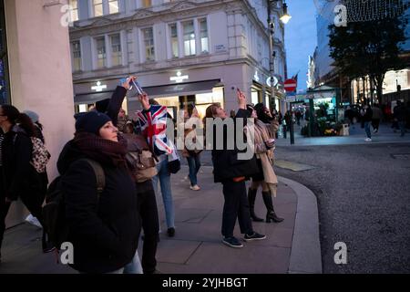 Touristen halten an und machen Fotos von den Weihnachtsfenstern und Weihnachtslichtern entlang der Old Bond Street, Mayfair, im Zentrum von London, England, Großbritannien Stockfoto