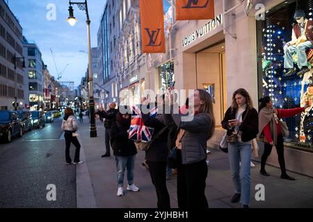 Touristen halten an und machen Fotos von den Weihnachtsfenstern und Weihnachtslichtern entlang der Old Bond Street, Mayfair, im Zentrum von London, England, Großbritannien Stockfoto