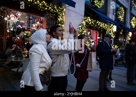 Touristen halten an und machen Fotos von den Weihnachtsfenstern und Weihnachtslichtern entlang der Old Bond Street, Mayfair, im Zentrum von London, England, Großbritannien Stockfoto