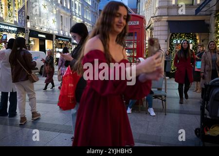 Touristen halten an und machen Fotos von den Weihnachtsfenstern und Weihnachtslichtern entlang der Old Bond Street, Mayfair, im Zentrum von London, England, Großbritannien Stockfoto