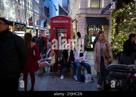 Touristen halten an und machen Fotos von den Weihnachtsfenstern und Weihnachtslichtern entlang der Old Bond Street, Mayfair, im Zentrum von London, England, Großbritannien Stockfoto