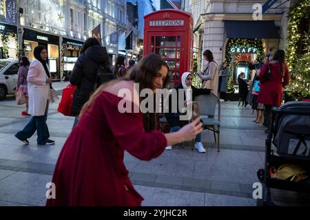 Touristen halten an und machen Fotos von den Weihnachtsfenstern und Weihnachtslichtern entlang der Old Bond Street, Mayfair, im Zentrum von London, England, Großbritannien Stockfoto