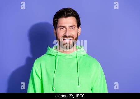 Foto-Porträt des gutaussehenden reiferen Alters funky lächelnder Mann trägt neongrüne Kapuzenpullover Sportswear isoliert auf violettem Hintergrund Stockfoto