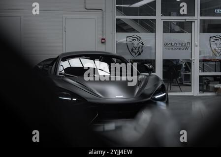 Ein mattschwarzer McLaren 720S parkt in einer gut beleuchteten, modernen Werkstatt. Die aerodynamische Form des Fahrzeugs und die LED-Scheinwerfer sind besonders hervorzuheben Stockfoto