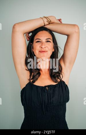 Frau in schwarzem Kleid mit erhobenen Armen, selbstbewusst lächelnd Stockfoto