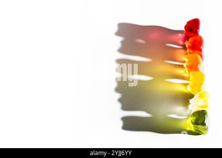 Eine Reihe von bunten Gummibären auf weißem Hintergrund, die lebendige Schatten erzeugen Stockfoto