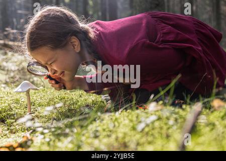 Kleines Mädchen erforscht Pilze mit Lupe im Wald Stockfoto