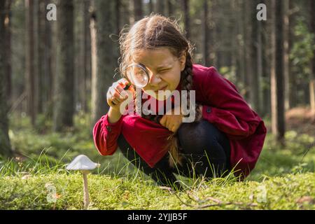 Kleines Mädchen erforscht Pilze mit Lupe im Wald Stockfoto