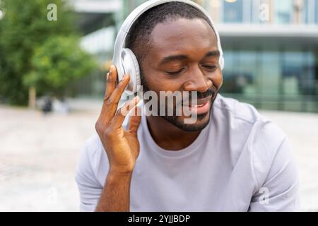 Musiksong-Konzept. Guter Start in den Tag. Glücklicher Afroamerikaner, der moderne Hit auf der Straße in der Stadt hört. Person Guy mit Kopfhörern genießen Sie Ihre Lieblingsmusik im Freien. Lebensfreude der Menschen Stockfoto