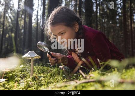 Kleines Mädchen erforscht Pilze mit Lupe im Wald Stockfoto