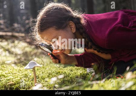 Kleines Mädchen erforscht Pilze mit Lupe im Wald Stockfoto