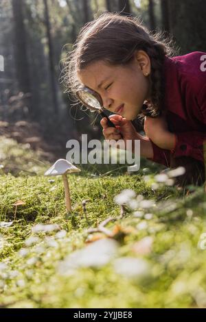 Kleines Mädchen erforscht Pilze mit Lupe im Wald Stockfoto