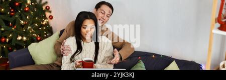 Ein liebevolles Paar entspannt sich während Weihnachten auf einer Couch, genießt Getränke und Gesellschaft. Stockfoto