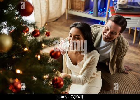 Ein liebevolles Paar teilt die Freude, wenn sie ihren Weihnachtsbaum zu Hause zusammen schmücken. Stockfoto