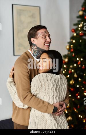 Ein liebevolles Paar, das sich in seinem gemütlichen Zuhause in einer warmen Umarmung umgeben von Weihnachtsdekorationen teilt Stockfoto