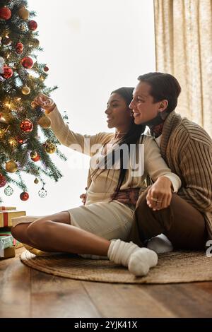 Ein liebevolles Paar sitzt zusammen und teilt Freude, während er seinen Weihnachtsbaum schmückt. Stockfoto