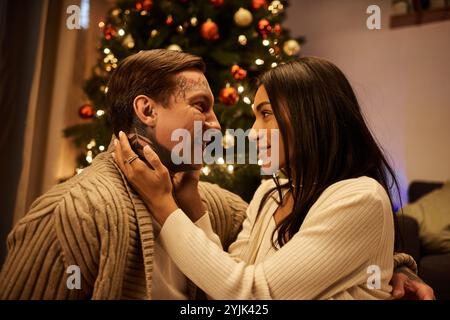 Ein liebevolles Paar teilt sich einen zärtlichen Moment zu Hause, umgeben von Weihnachtsdekoration und Lichtern. Stockfoto