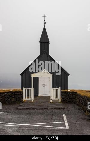 Schwarze Holzkirche mit einem Kreuz auf dem Turm. Weiße Details. Auf einer Weide, in der Nähe des Ozeans, auf einer Halbinsel gelegen. Budakirkja, Island. Stockfoto