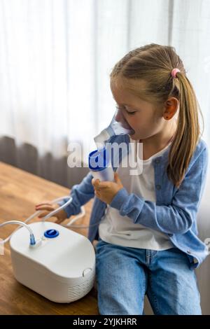 Zu Hause atmet ein 5-jähriges Mädchen durch einen Vernebler und konzentriert sich auf ihre Inhalationstherapie. Hochwertige Fotos Stockfoto