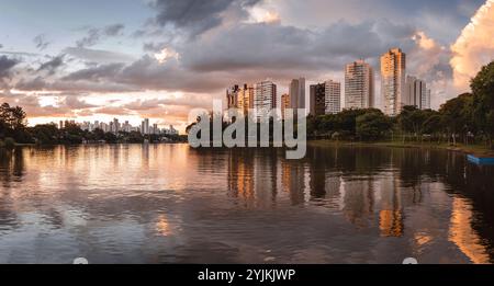 Urbane Szene in der Abenddämmerung mit hohen Gebäuden, die sich in einem See spiegeln, umgeben von Bäumen, unter einem teilweise bewölkten Himmel. Stockfoto