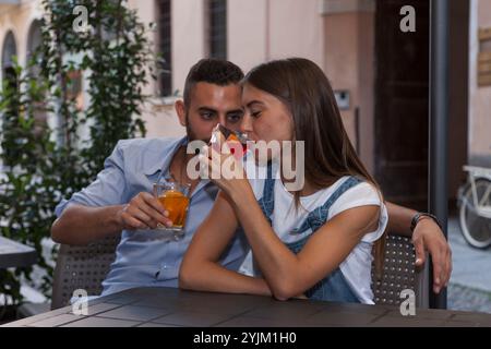 Wunderschönes Paar lächelnder junger Erwachsener, die Cocktails trinken, die an einem Tisch in einem Pub im Freien sitzen Stockfoto