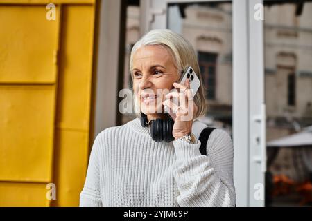 Eine schöne reife Frau mit grauem Haar lächelt, während sie mit Kopfhörern am Telefon spricht. Stockfoto