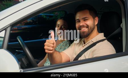 Glückliches kaukasisches Familienpaar, das im Auto sitzt Mann Mann Mann Fahrer schnallt Sicherheitsgurt lächelnd zeigt Daumen nach oben Geste Frau Mädchen Auto Stockfoto