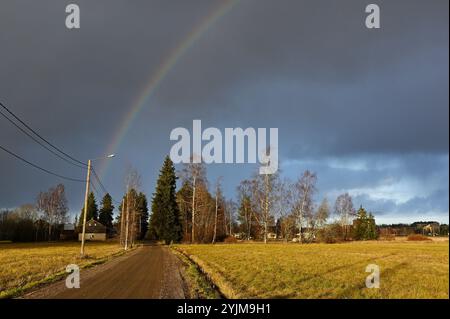 Eine ländliche Szene mit einer unbefestigten Straße, die sich durch eine Landschaft unter einem dramatischen Himmel zieht. Ein schwacher Regenbogenbogen über den Himmel sorgt für einen Hauch Stockfoto