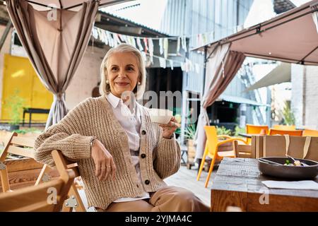 Diese elegante Frau mit grauen Haaren entspannt sich in einem Café und genießt ihren Tee in einer bezaubernden Umgebung. Stockfoto