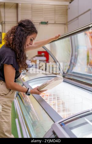 Frau mittleren Alters, die Tiefkühlprodukte in der Tiefkühlabteilung des Supermarktes auswählt Stockfoto