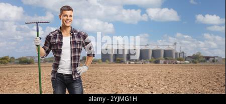 Junger Bauer, der einen Rechen auf einem Feld hält Stockfoto
