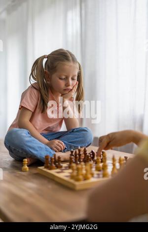 Das 5-jährige Mädchen spielt mit einem Mini-Schachset und konzentriert sich intensiv, während sie ihren nächsten Zug sorgfältig plant. Hochwertige Fotos Stockfoto