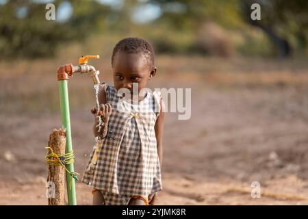 Mali,Kenia - Agust 19 2021:ein Dorf in afrika, kleiner Junge trinkt Wasser aus einem Brunnen oder Brunnen. Stockfoto