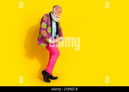 Foto in voller Größe von Rentner Mister tanzen Genießen Sie Spaß gekleidete stilvolle bunte rosa klassische Kleidung isoliert auf gelbem Hintergrund Stockfoto