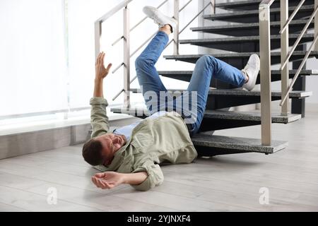 Verletzter Mann auf dem Boden im Gebäude nach dem Sturz von der Treppe. Gefährlicher Unfall Stockfoto