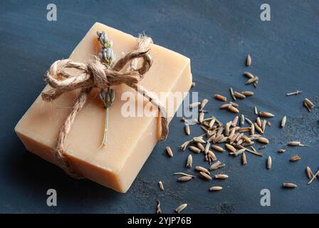 Hausgemachte frische Lavendelseife, wunderschön dekoriert mit einer rustikalen Schleife, platziert auf einem dunkelblauen Hintergrund, für eine natürliche und elegante Präsentation. Stockfoto