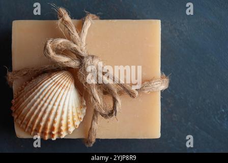 Hausgemachte Lavendelseife mit dekorativer Schleife und Muscheln auf dunklem Hintergrund für eine beruhigende, natürliche Szene. Stockfoto