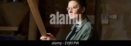 Eine gelernte Schreinerin konzentriert sich darauf, ein Holzstück in ihrer gut ausgestatteten Werkstatt zu Formen. Stockfoto